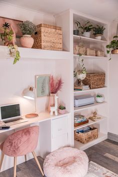 a white desk topped with a laptop computer sitting on top of a wooden floor next to a shelf filled with potted plants