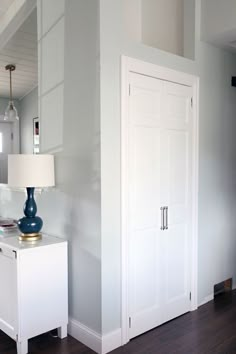 a room with white walls and wood flooring next to a lamp on a table