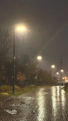 an empty street at night with lights on and rain coming down from the sky over it