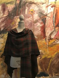 a mannequin wearing a black and red plaid ponchle in front of a painting