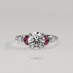 a diamond and ruby engagement ring on a white surface