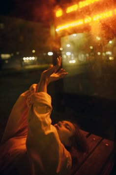 a woman laying on top of a wooden bench in front of a building at night