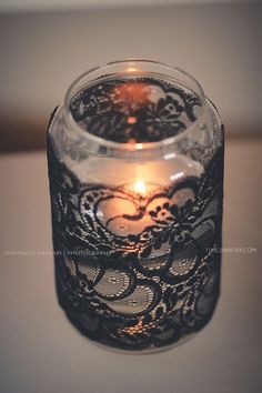 a lit candle in a glass jar with lace on the bottom and inside, sitting on a table