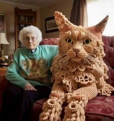 an elderly woman sitting on a couch next to a crocheted cat that looks like it's made out of yarn