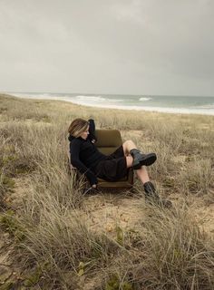 a woman sitting in a chair on the beach with her feet up and head down