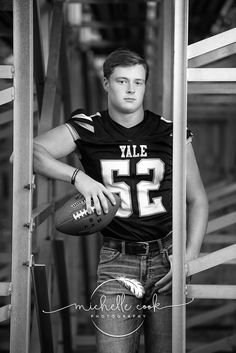 a young man holding a football standing next to a metal structure with stairs in the background