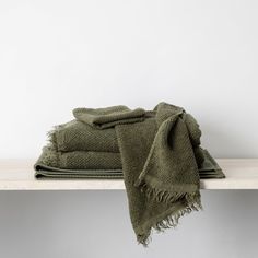 two folded green towels sitting on top of a wooden shelf next to a white wall