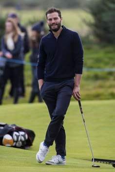 a man with a golf club walking towards the green on a golf course while people look on