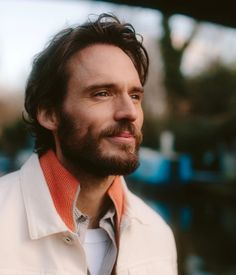 a close up of a person wearing a white jacket and an orange shirt with a beard