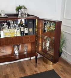 a wooden cabinet filled with bottles and glasses on top of a hard wood floor next to a potted plant