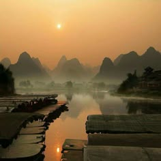 boats are lined up on the water in front of mountains and foggy sky at sunset