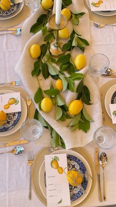 the table is set with plates, silverware and yellow lemons on top of each plate