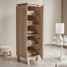 an open cabinet in the corner of a room with a white chair and table next to it