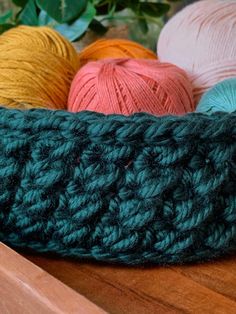 three balls of yarn sitting on top of a wooden table next to green leaves and flowers