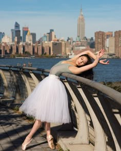 a woman in a white tutu posing on a bridge with her arms stretched out