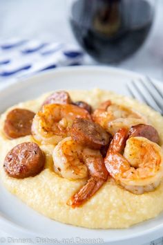 a white plate topped with shrimp and grits on top of a table next to a fork