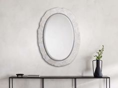 a white oval mirror sitting on top of a black table next to a vase with a green plant