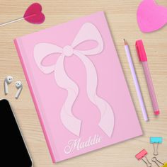 a pink notebook with a bow and name on the cover next to some other items