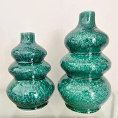 two green vases sitting on top of a glass table