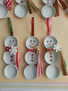 snowman ornaments are hanging on the wall in front of plates and spoons with ribbons around them