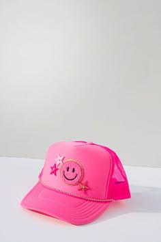 a pink trucker hat with a smiley face and stars on the front, sitting on a white surface