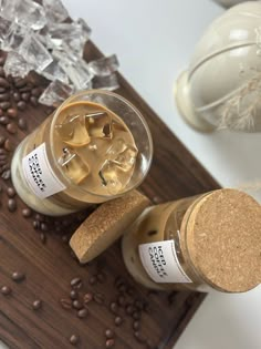 two jars filled with ice and coffee beans on top of a wooden cutting board next to some glassware