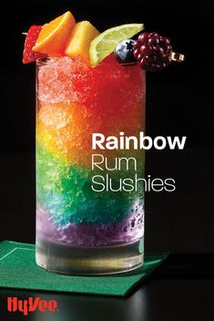 a rainbow drink in a tall glass with fruit on top