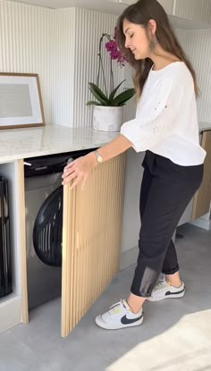 a woman standing in front of a washer with her hand on the door handle