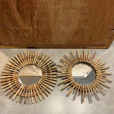 two circular mirrors sitting next to each other on top of a cement floor in front of a wooden door