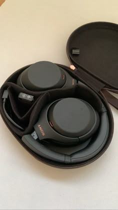 two black headphones sitting in a case on top of a white table next to a pair of glasses