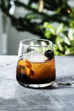 a glass filled with ice sitting on top of a table next to a pine tree