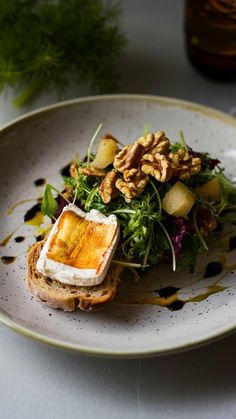 a white plate topped with toasted bread covered in greens and nuts next to a glass of wine