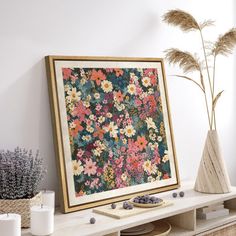 a vase with some flowers in it next to a painting on a shelf and candles