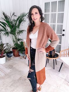 a woman standing in front of a door wearing a cardigan sweater and ripped jeans