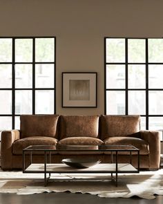 a living room scene with focus on the couch and coffee table in front of large windows