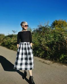 a woman standing on the side of a road wearing a black and white checkered skirt