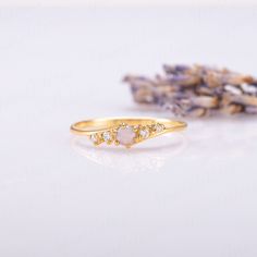 a yellow gold ring with three diamonds on it and lavender flowers in the foreground