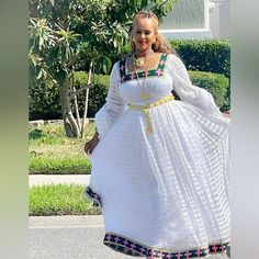 Ethiopian And Eritrean Traditional Dress (Habesha Kemis The Dress Is White With A Textured Pattern And Features Decorative Elements In Green And Pink Around The Neckline, Cuffs, And Hem. The Design Seems To Be Traditional Or Cultural, Possibly From A Specific Region Or Ethnic Background. The Dress Also Includes Long Sleeves Ethnic Background, Ethiopian Dress, Petite Midi Dress, Habesha Kemis, Shoulder Ruffle Dress, Long Sleeve Print Dress, Mini Sweater Dress, Decorative Elements, Puffed Sleeves Dress