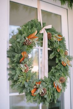 a wreath with pine cones and oranges hanging on the front door to welcome guests