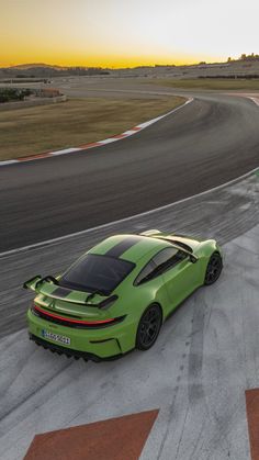 a green sports car driving on a race track at sunset or sunrise with the sun setting in the background