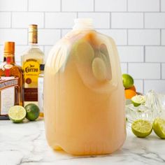 a jug filled with liquid sitting on top of a counter next to limes and bottles