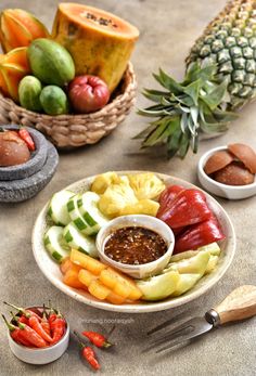 a plate full of fruit and vegetables on a table with pineapples in the background