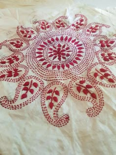 a red and white table cloth with an intricate design in the center, on top of a bed