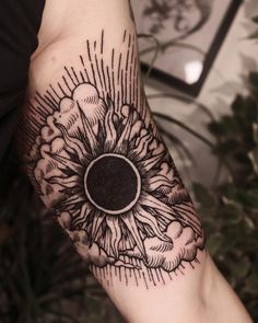 a black and white photo of a sunflower tattoo on the left arm, with clouds in the background