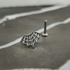 a pair of silver earrings sitting on top of a gray floor next to a screw