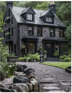 a stone house with black shingles and windows on the front, surrounded by greenery