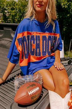 - Show off your team spirit in this dazzling oversized 'TOUCHDOWN' tee! Featuring a sequined design and chic unfinished seam accents, you'll shine on game day. Show your team spirit with our vibrant clothing collection inspired by the bold colors of popular college football teams like the Auburn Tigers and the University of Florida Gators. - Unlined lightweight material with unfinished seam accents - A sequined 'TOUCHDOWN' design across the front - Short drop sleeves - An oversized silhouette th Cheap Sports Shirt With Letter Print, Auburn College Football Game Outfit, Cheap Blue Tops With Team Logo, Collage Game Day Outfit, College Football Outfits For Women, Football T Shirt Ideas, Blue Varsity Tops For Game Day, Blue Top For College Football Season, Florida Gators Gameday Outfits