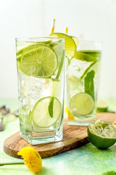 two glasses filled with lemon and limeade on top of a wooden cutting board next to an orange slice