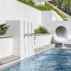 an outdoor swimming pool with water features and plants on the side, surrounded by white walls