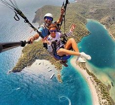 two people parasailing over an island in the middle of the ocean, with water and land around them